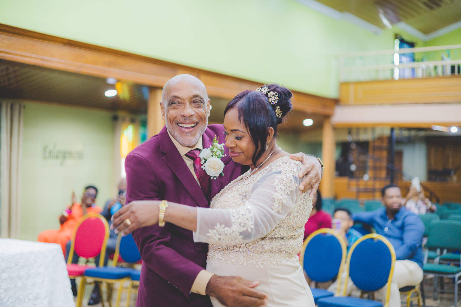 A smiling groom in a burgundy suit embracing his bride at their church ceremony