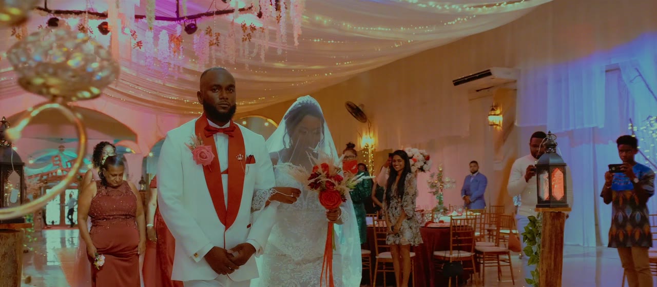 A bride and groom walking in together through a decorated reception hall, guests either side